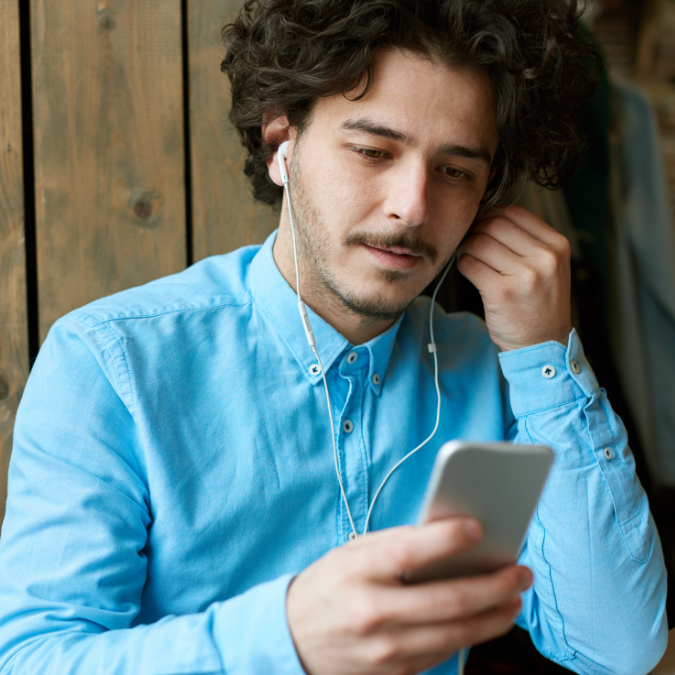 young man putting in earphones connected to his mobile phone as he awaits a phone call from an Affordable Counselling Solutions focused therapist