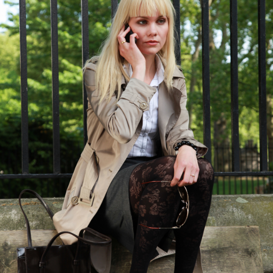 woman sitting against a park fence listening to an Affordable Counselling Solutions therapist on her mobile phone