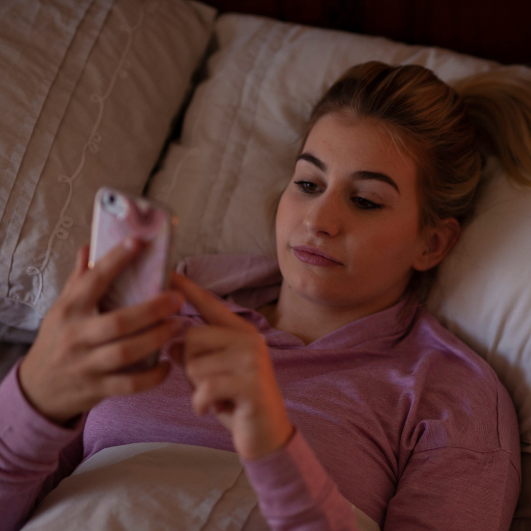 young woman laying in bed at bedtime booking online therapy from her mobile phone